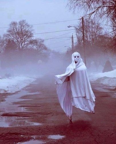 a ghostly woman walking down a street in the snow with her arms wrapped around her body