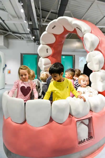 children are playing in a fake toothbrush at the dentist's office as adults look on