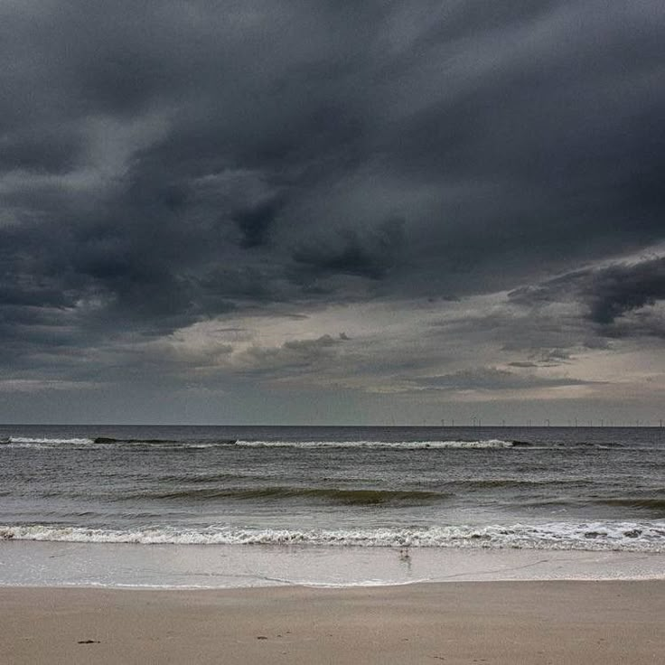 an ocean view with dark clouds over the water and people walking on the beach in the distance