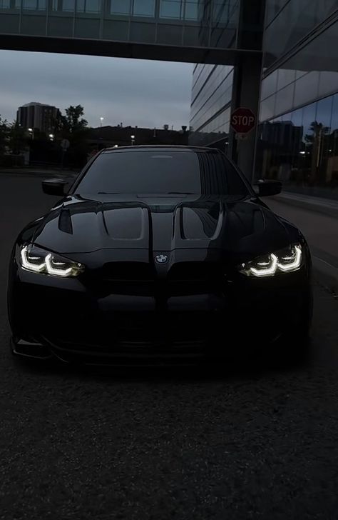 a black sports car parked in front of a tall building at night with its lights on