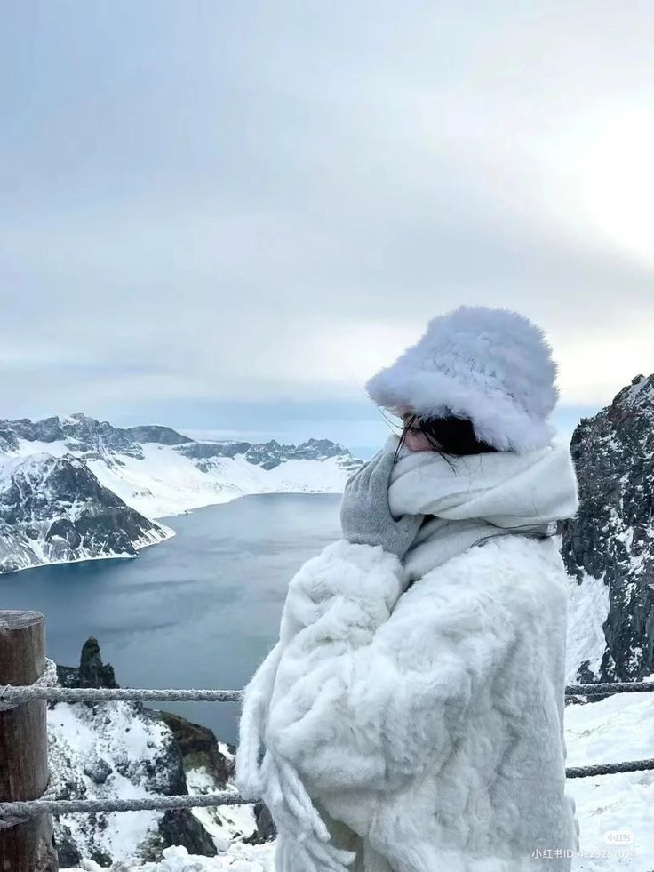 a woman standing on top of a snow covered mountain next to a body of water