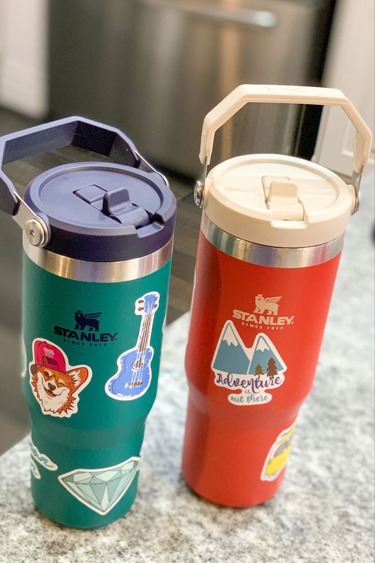 two travel mugs sitting next to each other on a counter