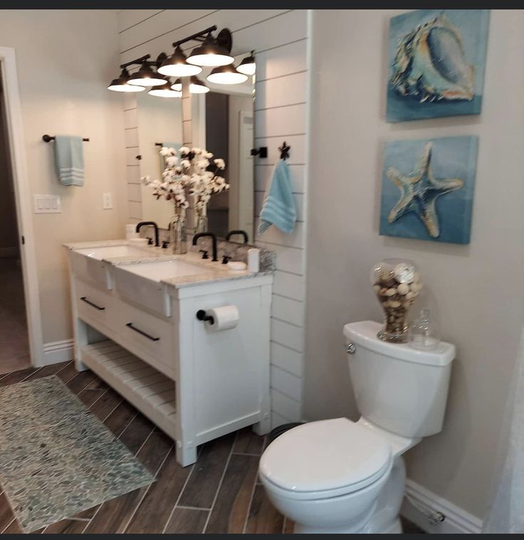 a white toilet sitting next to a sink in a bathroom under two pictures on the wall