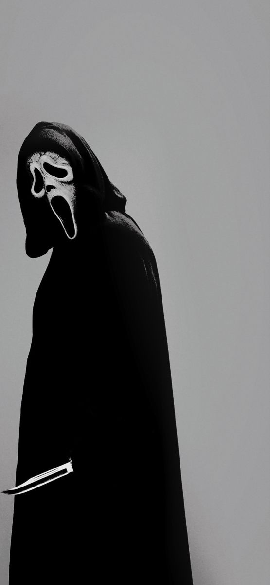 a man in a mask and cape holding a knife with his mouth wide open while standing against a gray background