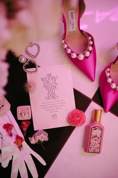 pink shoes and accessories are laid out on the floor next to a card, perfume bottle, and brochure