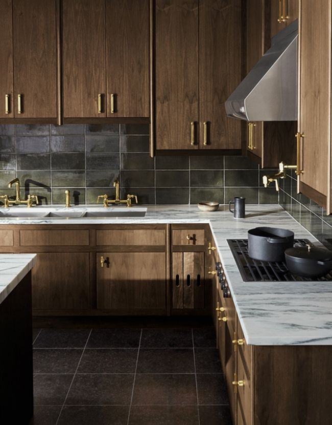 a kitchen with marble counter tops and wooden cabinets, gold pulls on the faucets