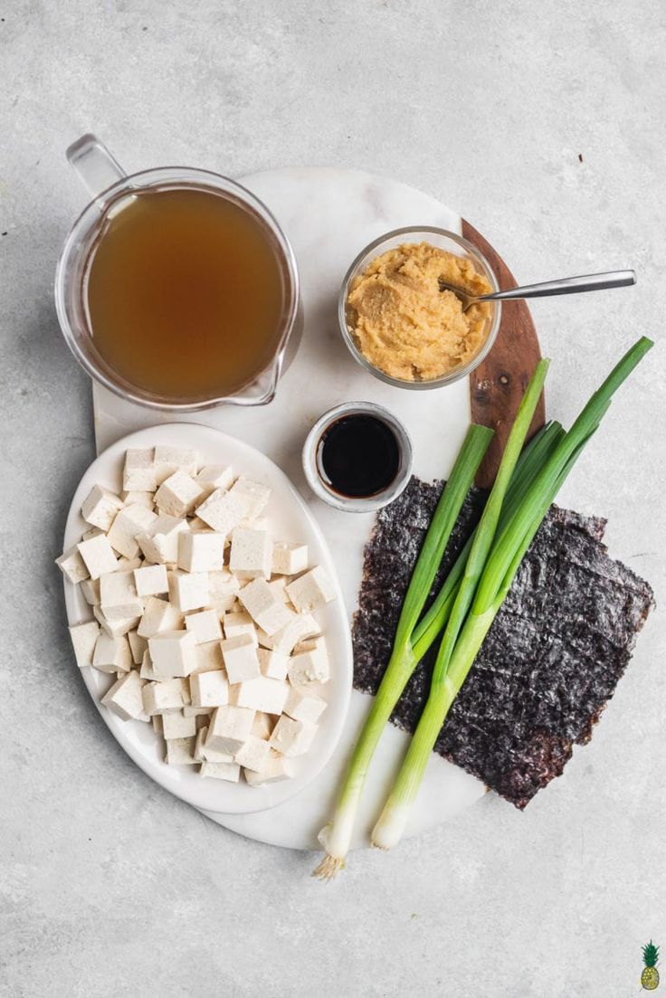 an assortment of food on a plate with sauces and green onions next to it