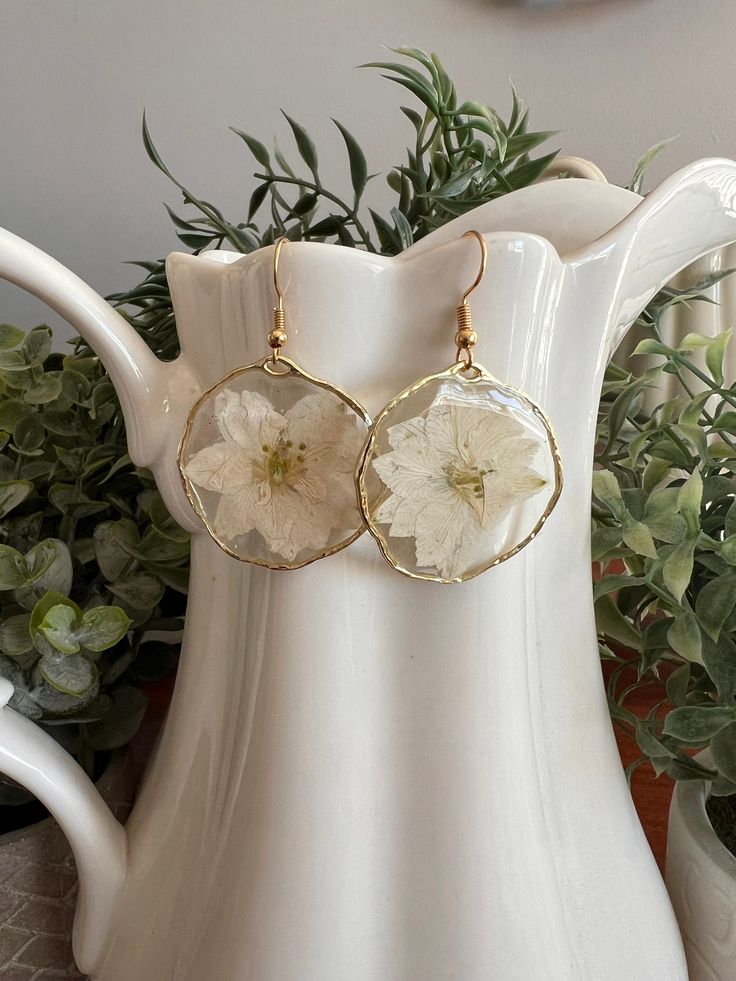 a pair of earrings with flowers on them sitting in front of a potted plant