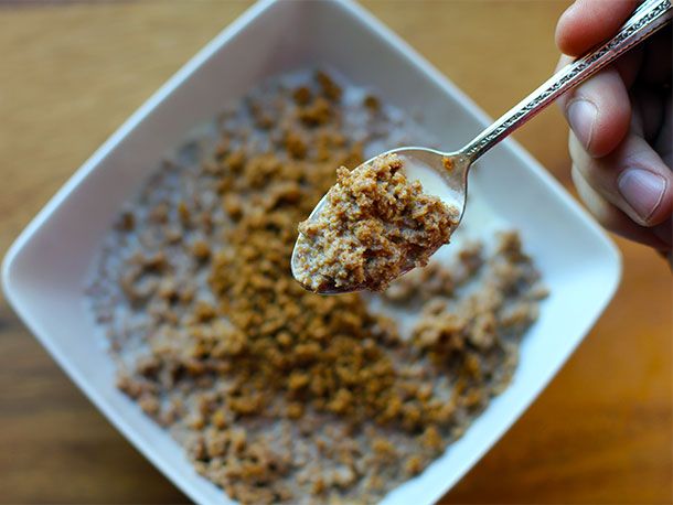 a person holding a spoon full of oatmeal in a white bowl on top of a wooden table