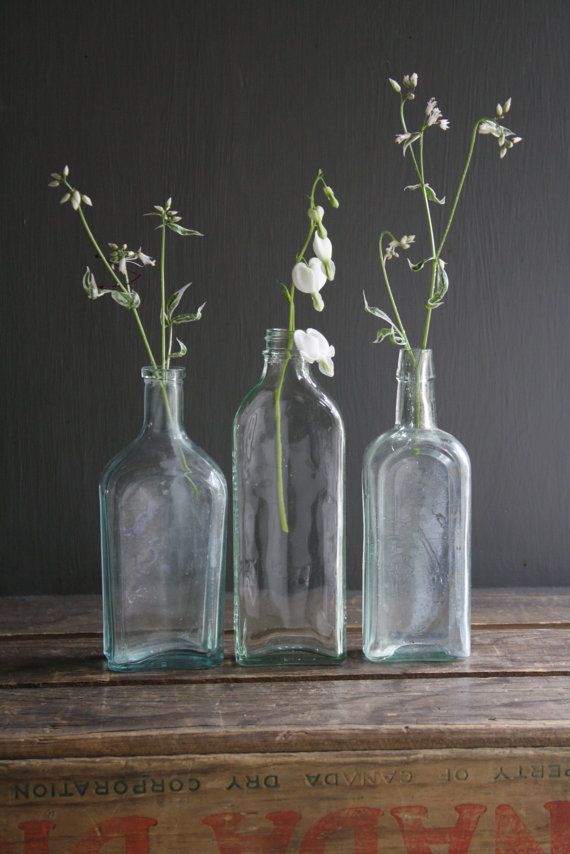 three glass bottles with flowers in them sitting on a wooden table next to an old box