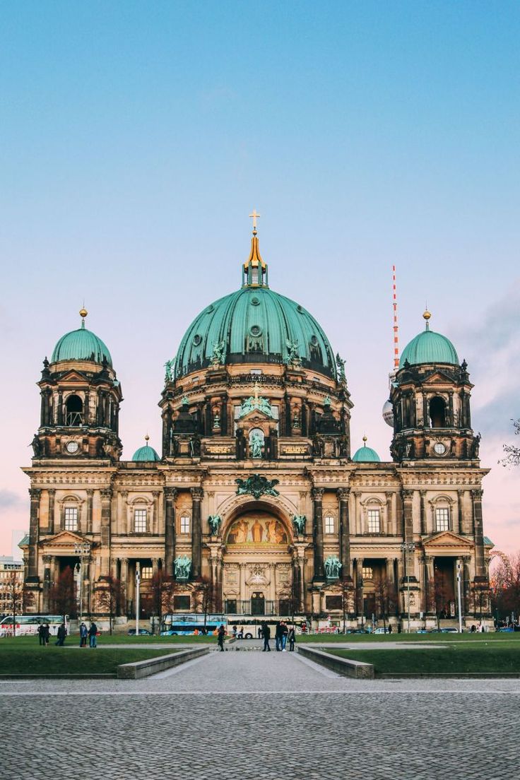 a large building with green domes on it's sides and people walking in front