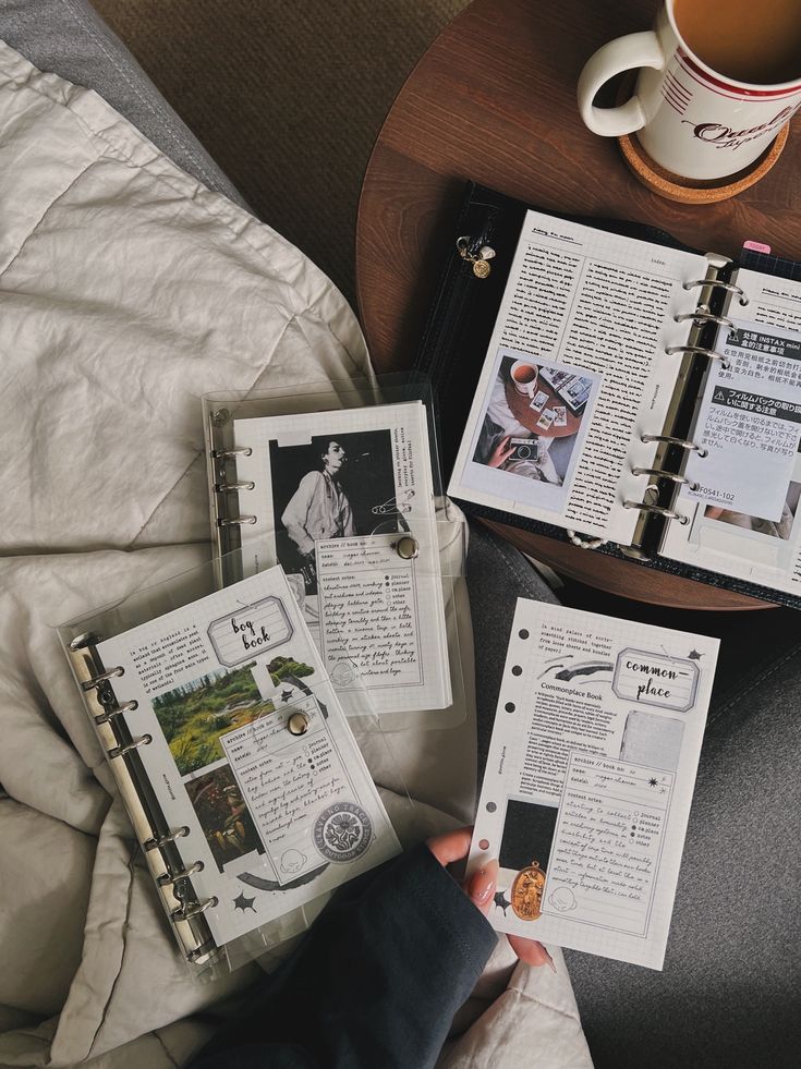 a person holding an open book next to a cup of coffee and papers on a bed