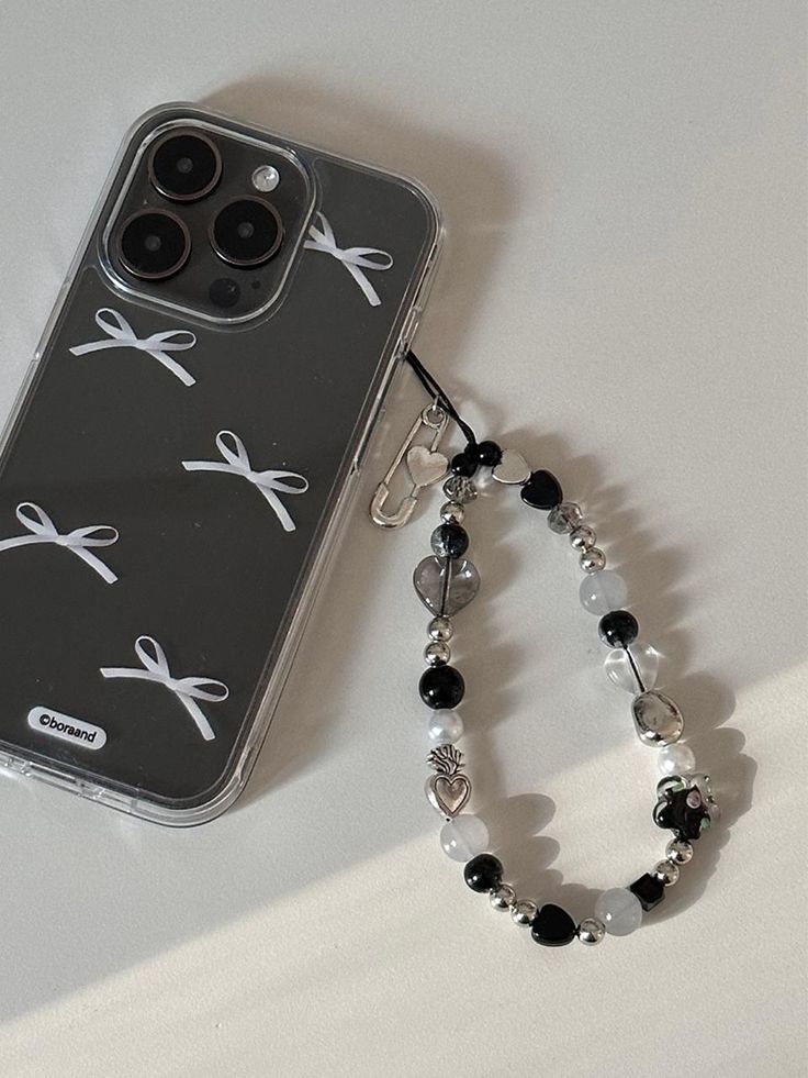 a cell phone case with scissors and beads attached to it on a white surface next to a bracelet