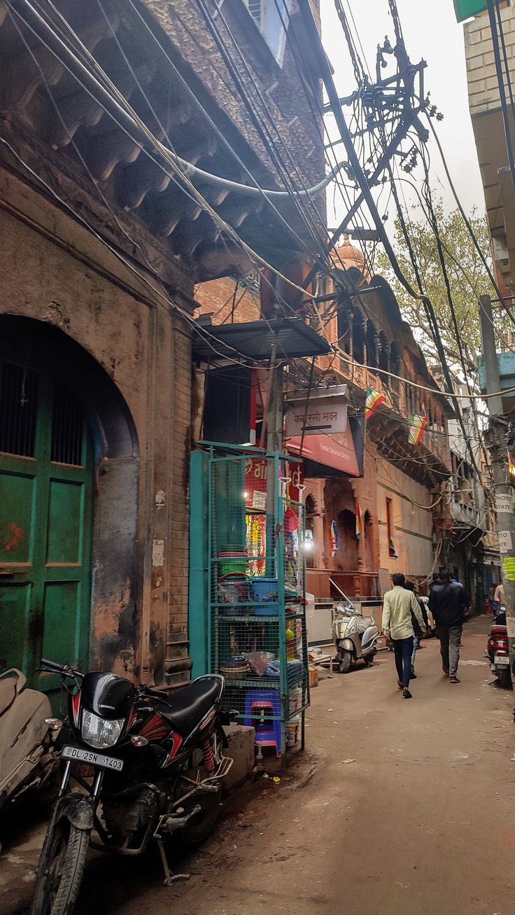 two people walking down an alley way with scaffolding on the buildings and motorcycles parked in front