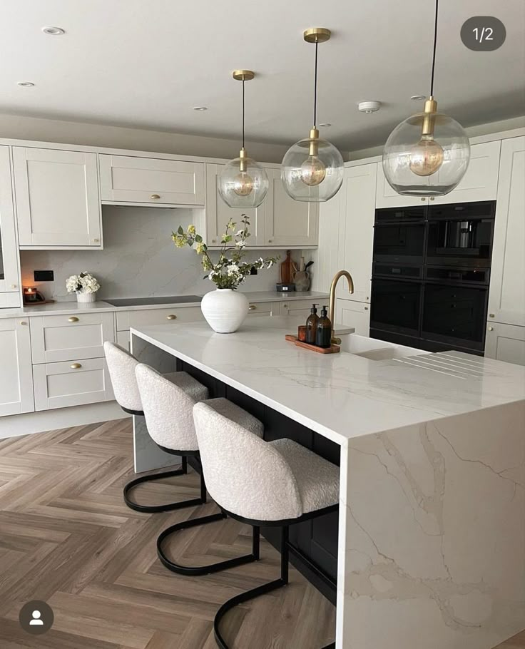 a large kitchen with marble counter tops and white cabinets, along with four bar stools