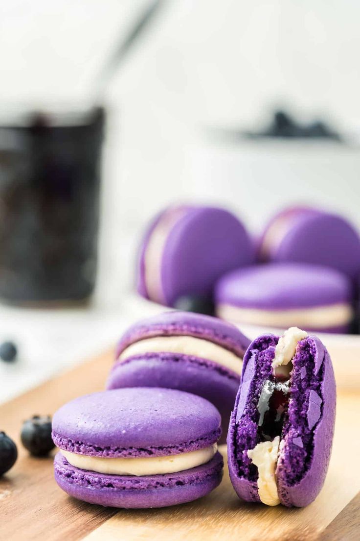 purple macaroons are cut in half on a cutting board next to blueberries