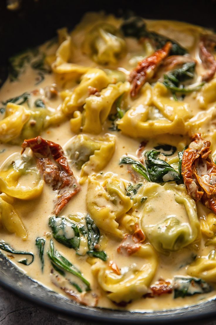 a pan filled with pasta and spinach covered in cheese sauce on top of a wooden table