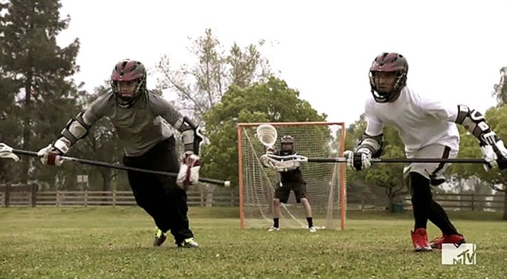 two men playing lacrosse on a field with trees in the background and red border around them