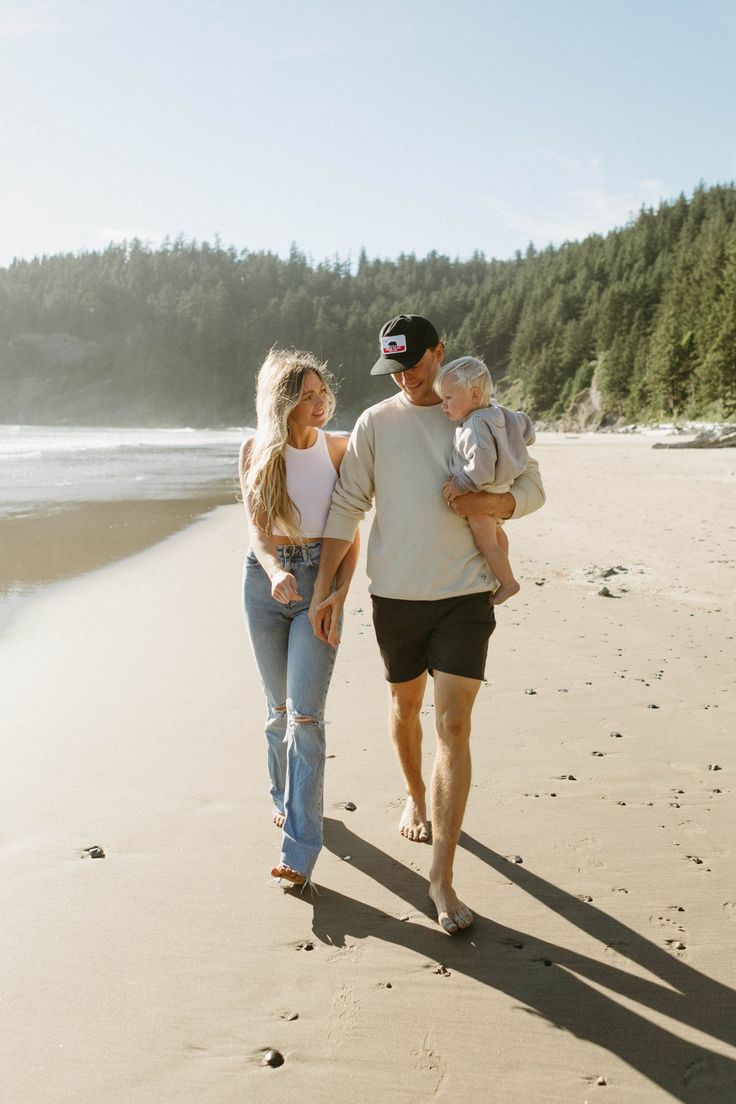 a man and woman walking on the beach with a baby in their arms while holding onto each other's hands