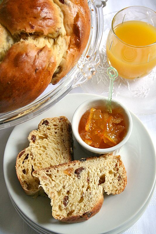 bread, jam and orange juice on a white tablecloth with a bowl of fruit