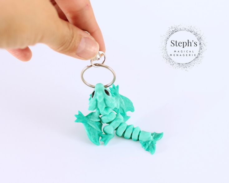 a hand holding a keychain that is shaped like a seahorse with green frosting on it