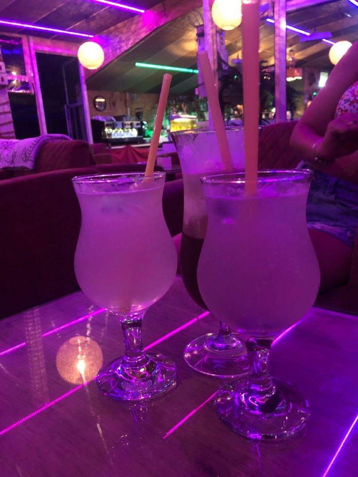 two drinks sitting on top of a table next to each other in front of a purple light