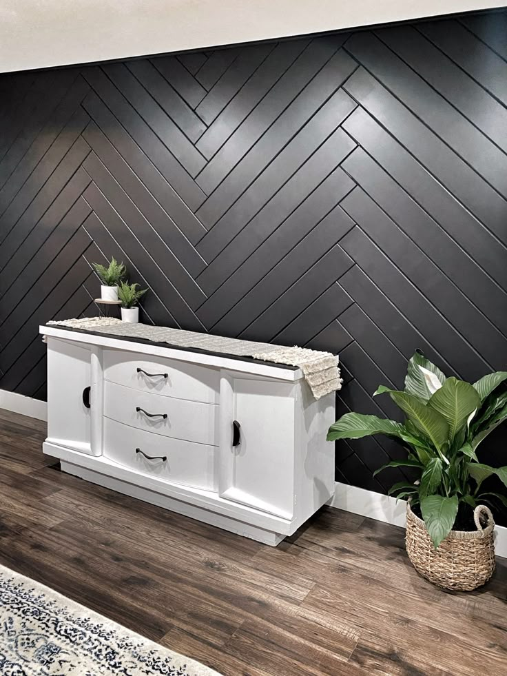 a living room with black and white herringbone wallpaper, two planters on either side of the tv stand