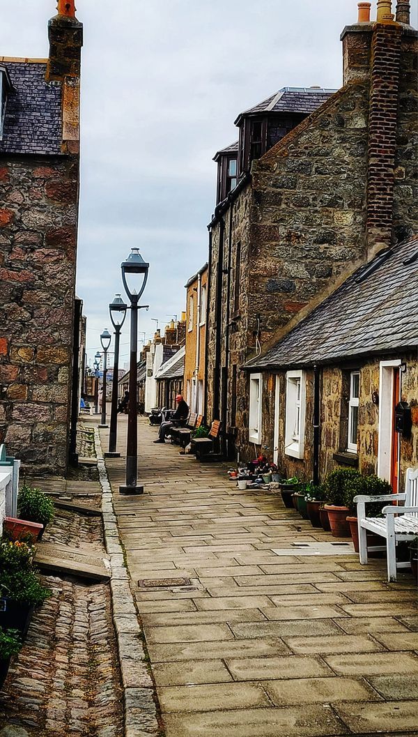 an empty street lined with stone buildings and benches next to each other in front of a lamp post