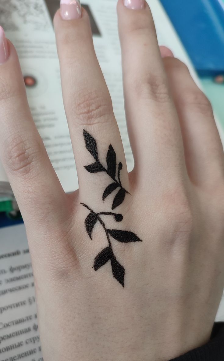 a woman's hand with a small black leaf tattoo on her left ring finger