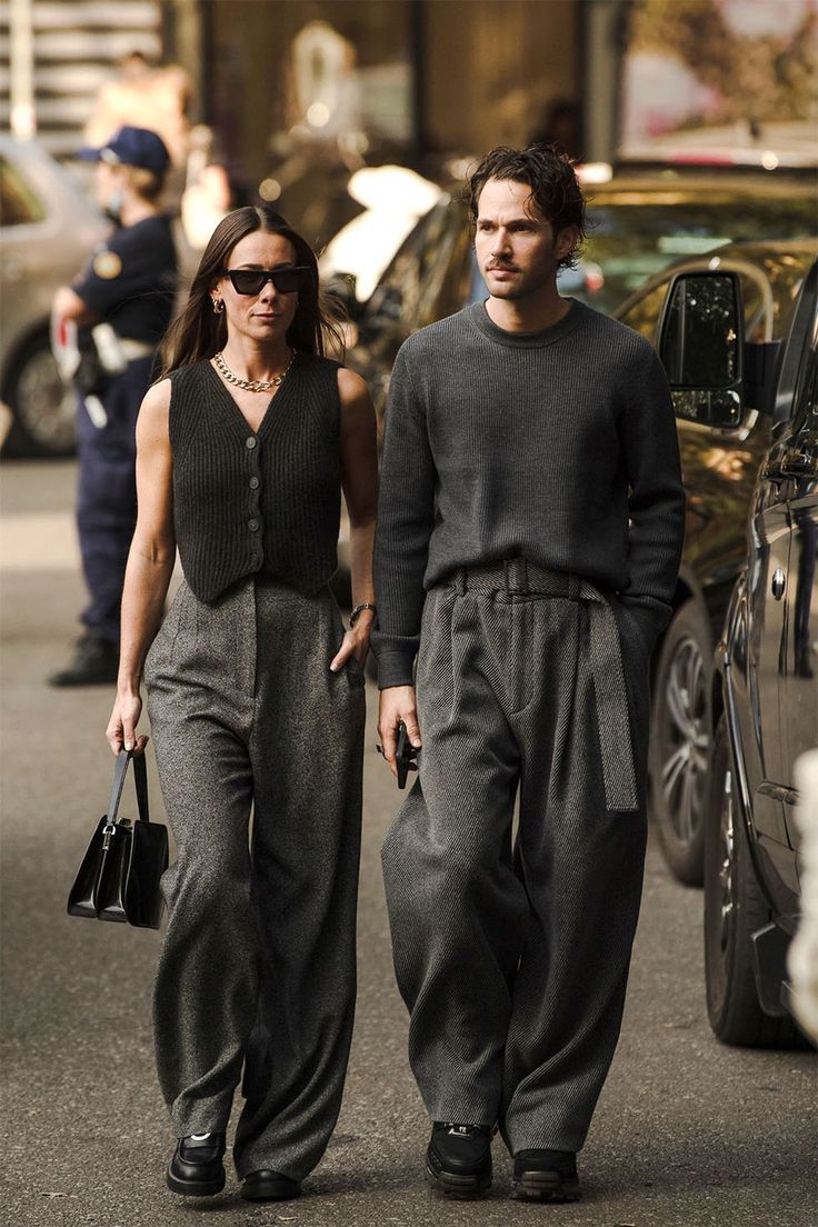 a man and woman walking down the street with cars in the backgrouds