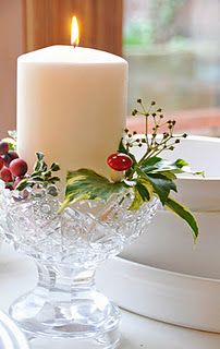 a lit candle sitting on top of a glass bowl filled with berries and greenery