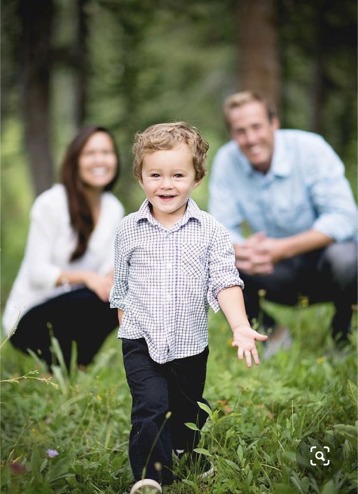 a little boy walking through the grass with his parents