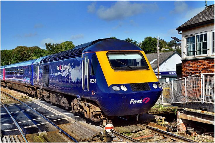 a blue and yellow train traveling down tracks next to a brick building on the other side