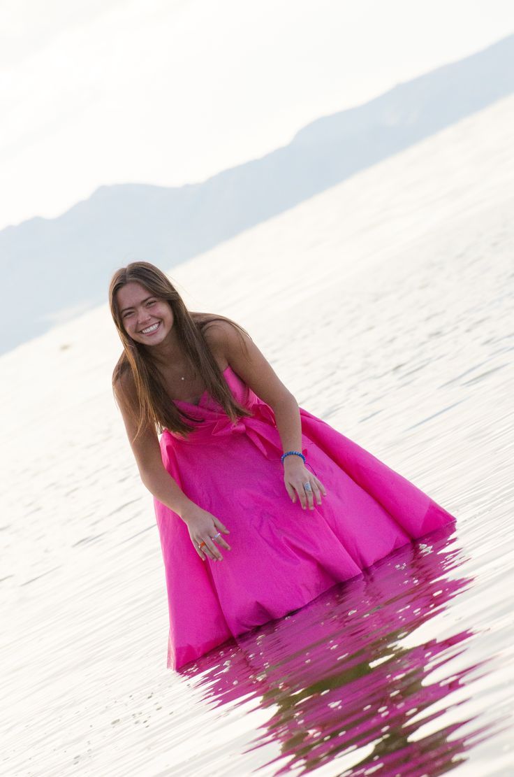 a woman in a pink dress standing in the water with her hands on her hips