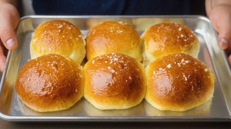 a person holding a metal tray with four rolls on it and one bun in the middle