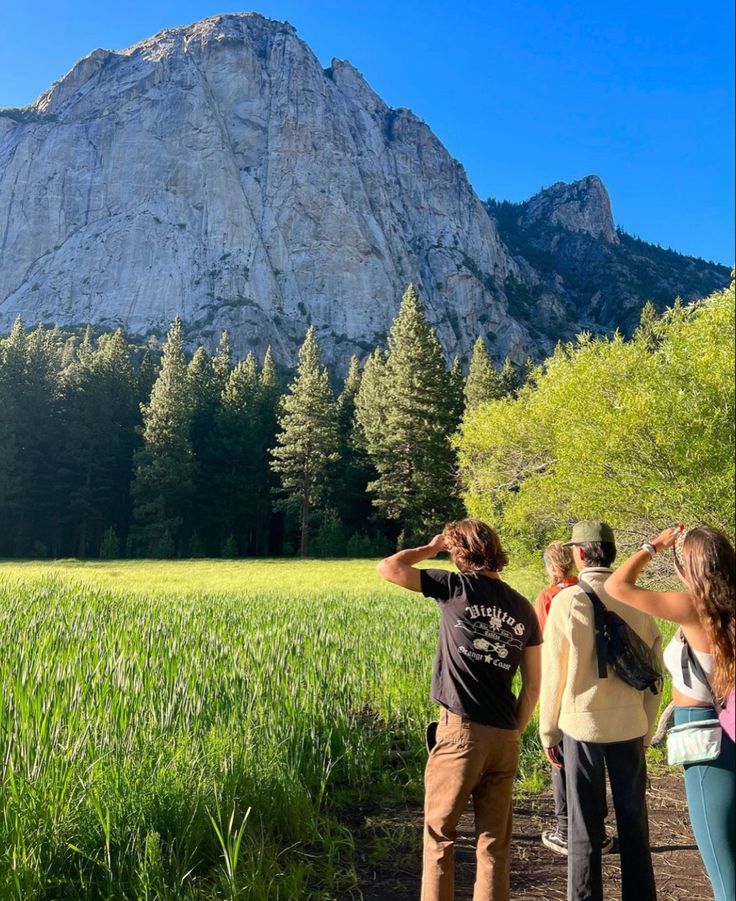 three people standing on a path looking at the mountains in the distance with trees and grass