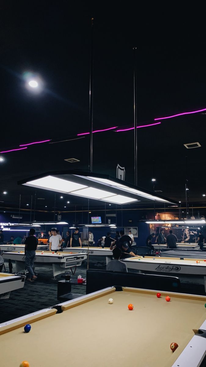 a pool table with several balls on it and people playing in the background at night