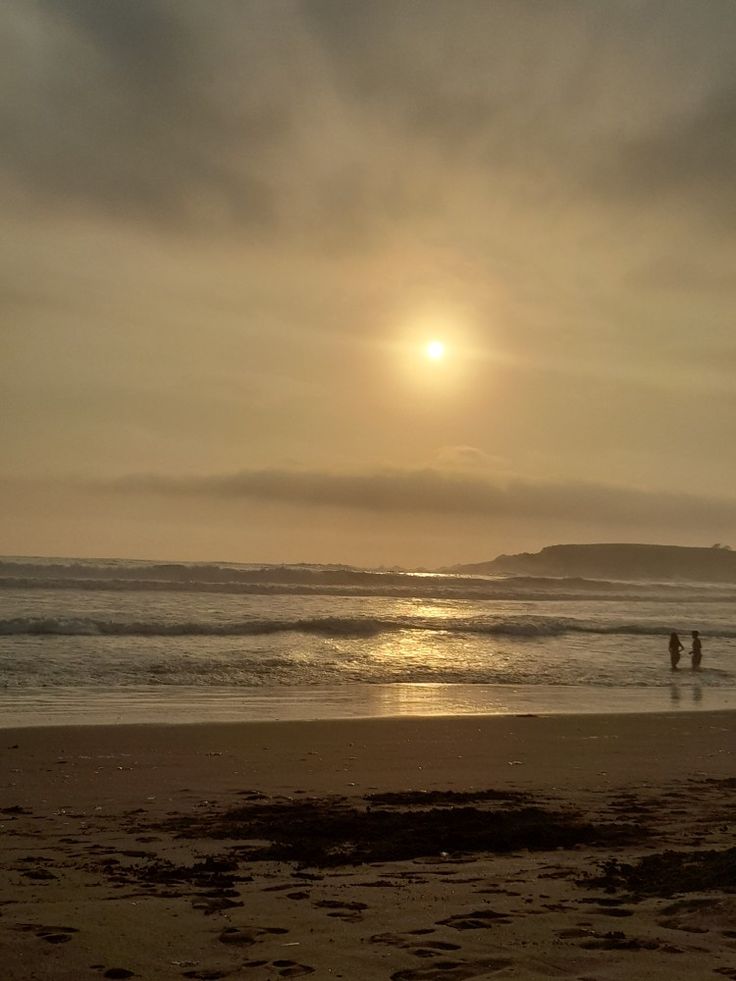 two people walking on the beach at sunset