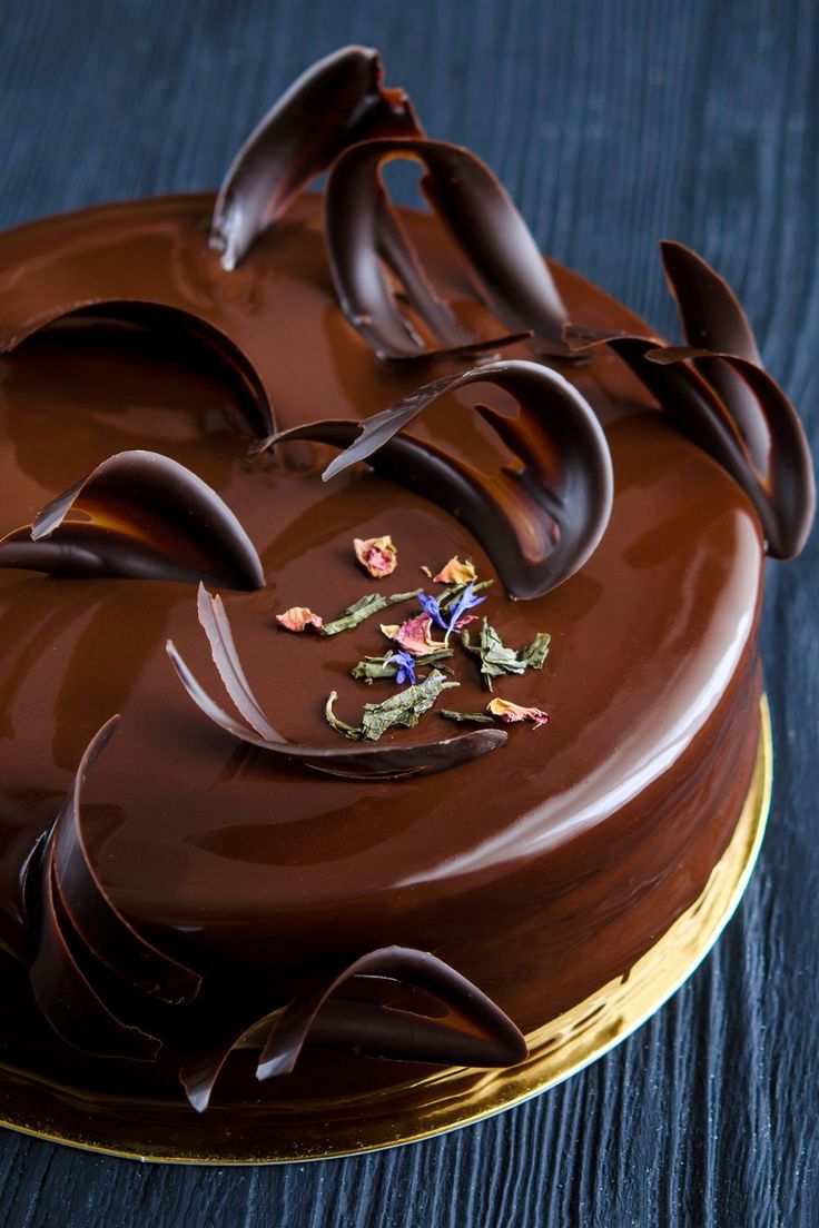 a chocolate cake on a gold platter with flowers and leaves in the top layer