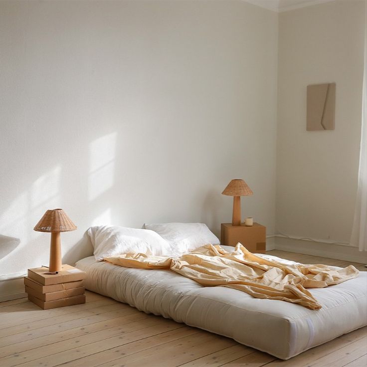 an unmade bed sitting on top of a hard wood floor next to a window