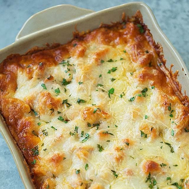 a casserole dish with cheese and parsley in it on a blue surface