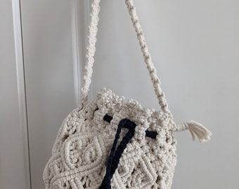 a white crocheted bag hanging from a hook on a door handle with a black tassel