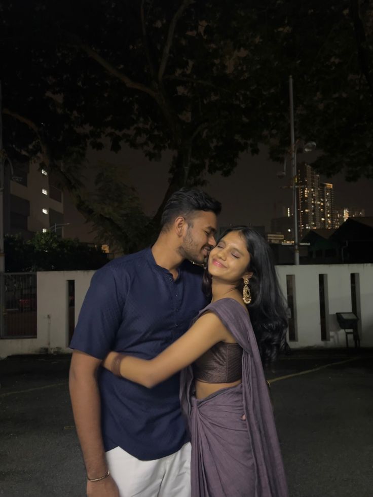 a man and woman standing next to each other in front of a tree at night