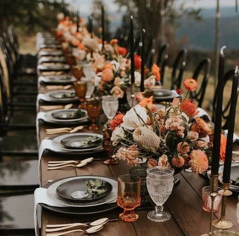 a long table set with place settings and flowers in vases on the top, along with candles