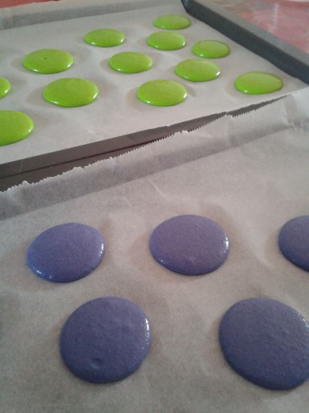 purple and green cookies sitting on top of wax paper in front of a baking sheet