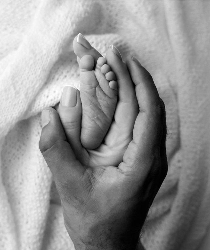 a black and white photo of a person holding a baby's foot in their hands