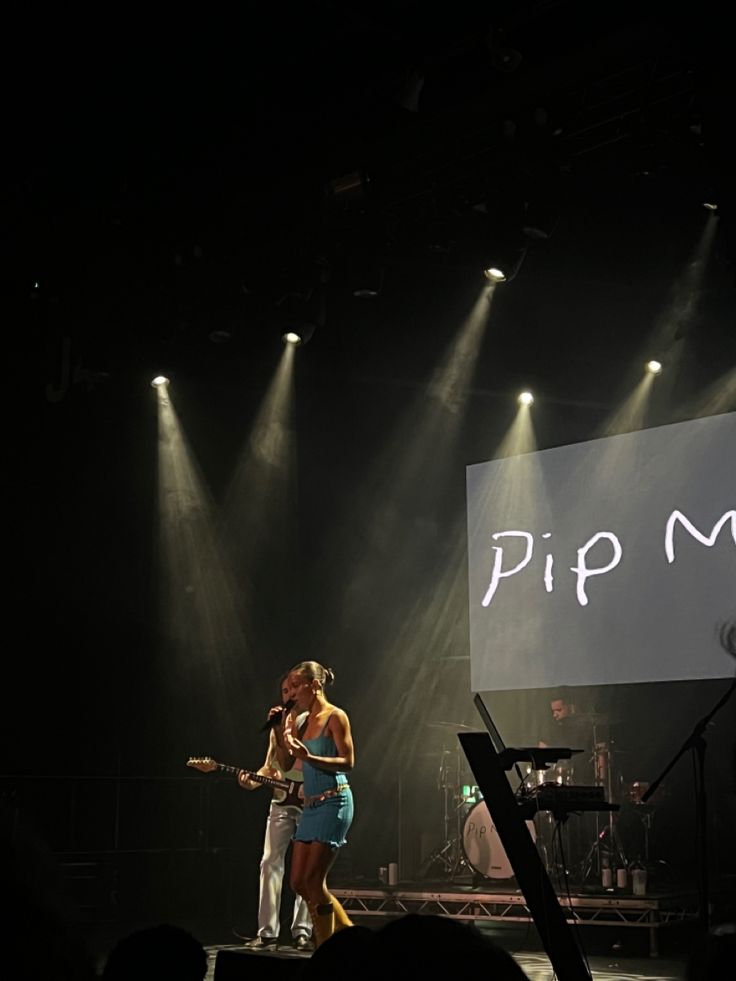 two women on stage with microphones in front of them, one holding a guitar and the other singing