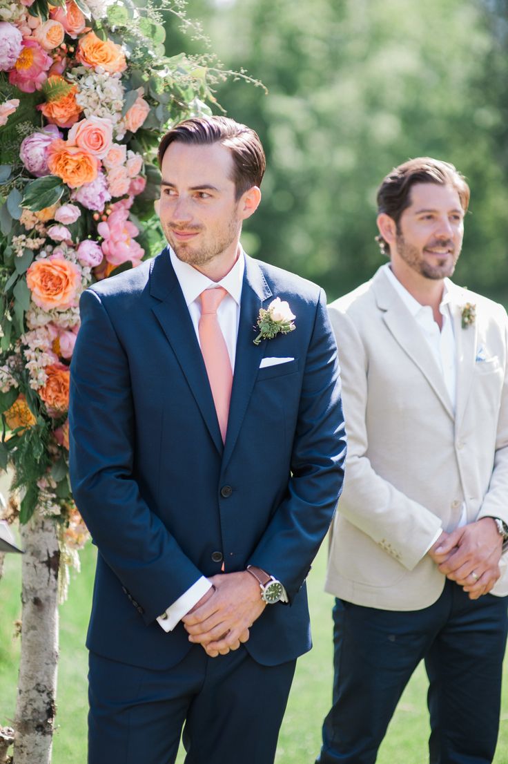 two men standing next to each other in front of a flower covered arbor with orange and pink flowers