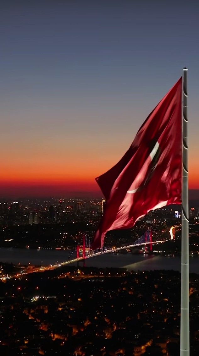 a large red flag flying over a city at night with the sun setting in the background