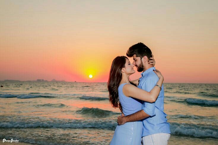 a man and woman are kissing on the beach at sunset, with the sun setting in the background